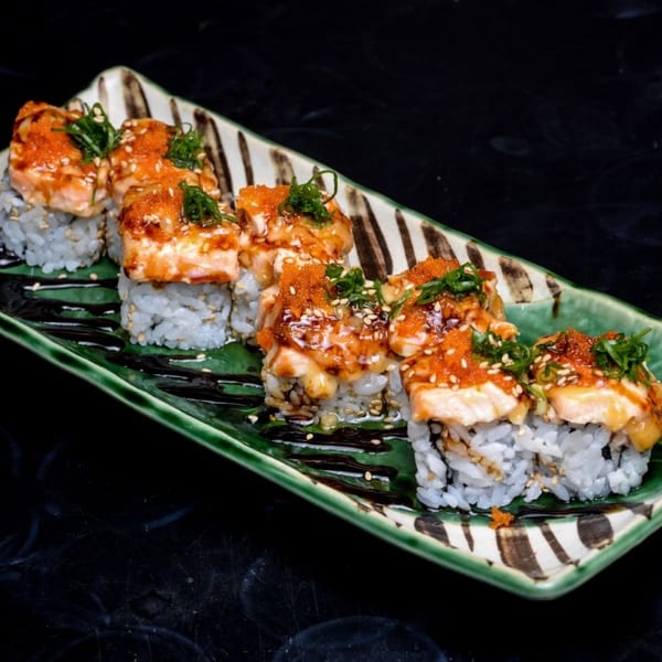 Sushi rolls topped with seared salmon, orange roe, and green garnish on a patterned green plate.