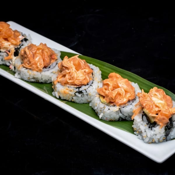 Five sushi rolls with spicy orange topping, served on a white plate with a green leaf.
